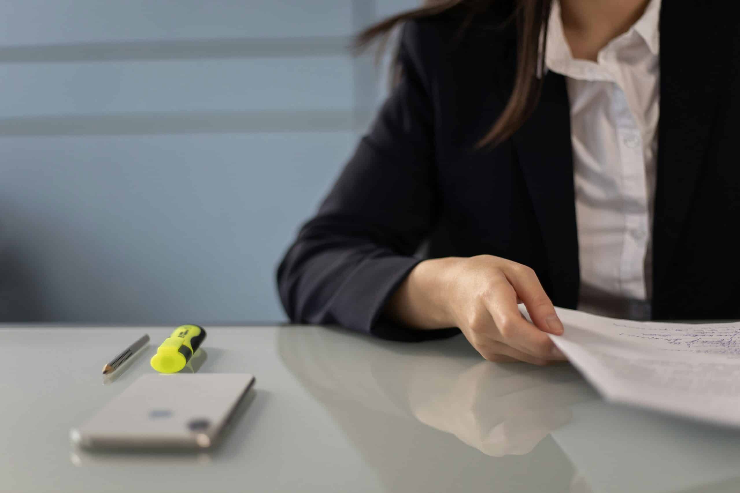 A person in a business suit reviewing a document at a desk with a pen, highlighter, and smartphone in the foreground.