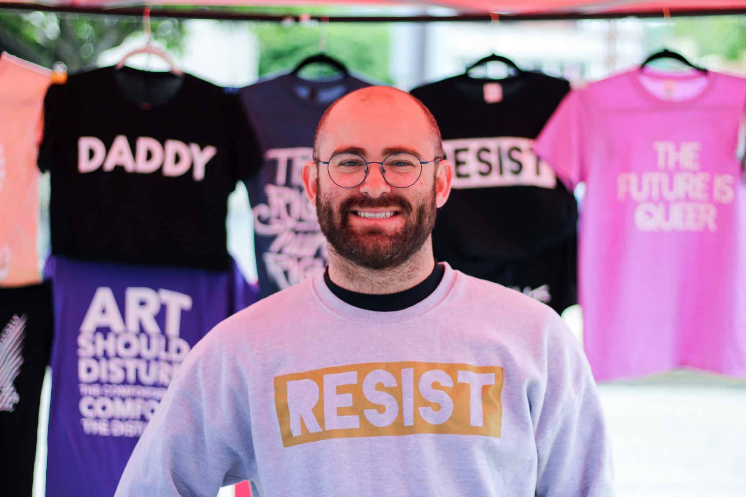 A refugee, eager to succeed, runs a T-shirt business with a hopeful smile, representing the resilience and determination of refugees.