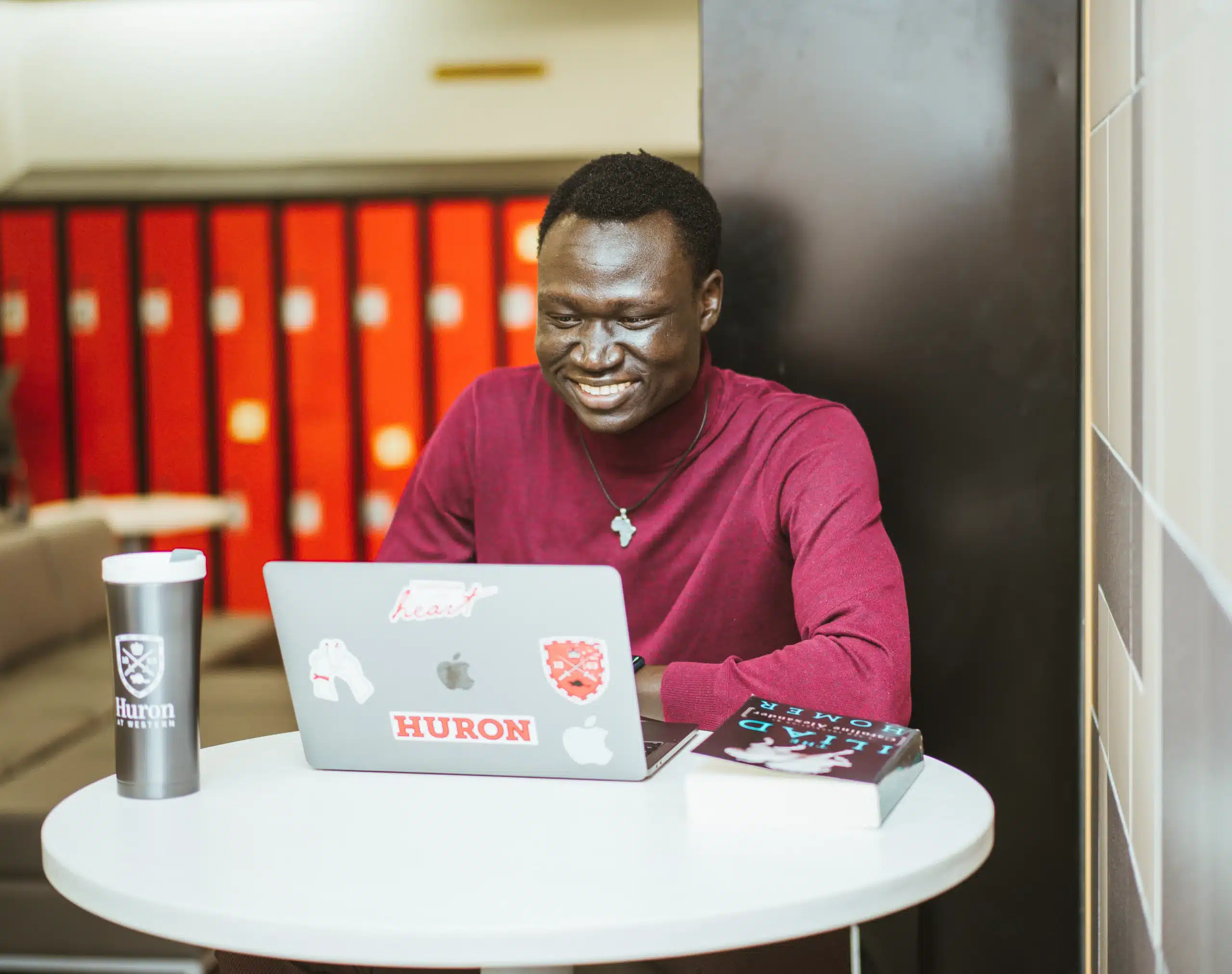 Nhial, a refugee student and youth advocate, stands on the campus of Huron University in Canada during his second year of studies. He appears confident and reflective, surrounded by a university setting that symbolizes growth and opportunity.