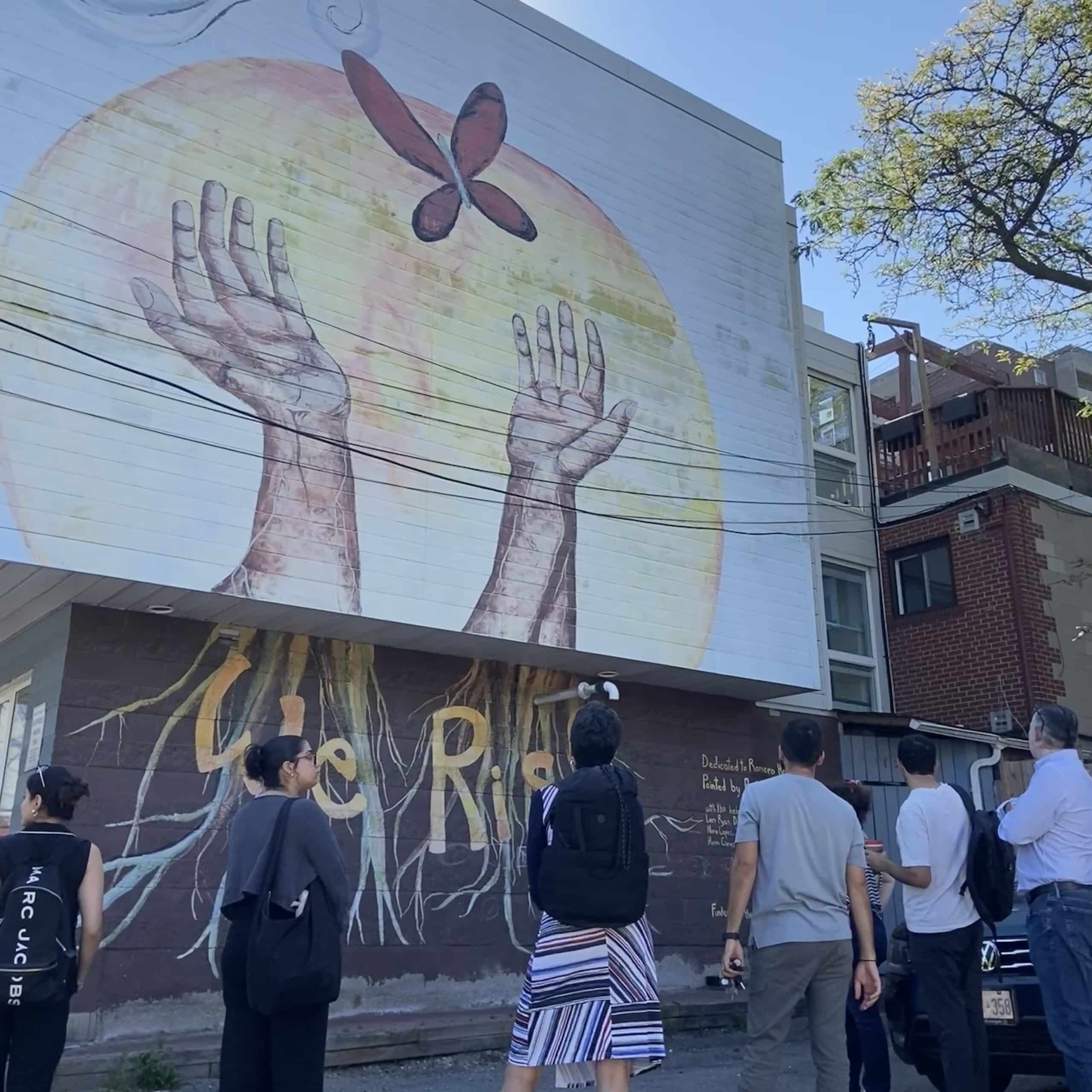 Jumpstart team viewing the mural at the back of the Romero House office building, symbolizing how Romero House uplifts and empowers the refugee community to rise.