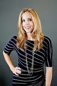 Professional headshot of Denise Robertson, Partner at Mills & Mills LLP, wearing a navy striped dress with a silver necklace, smiling confidently against a neutral gray background