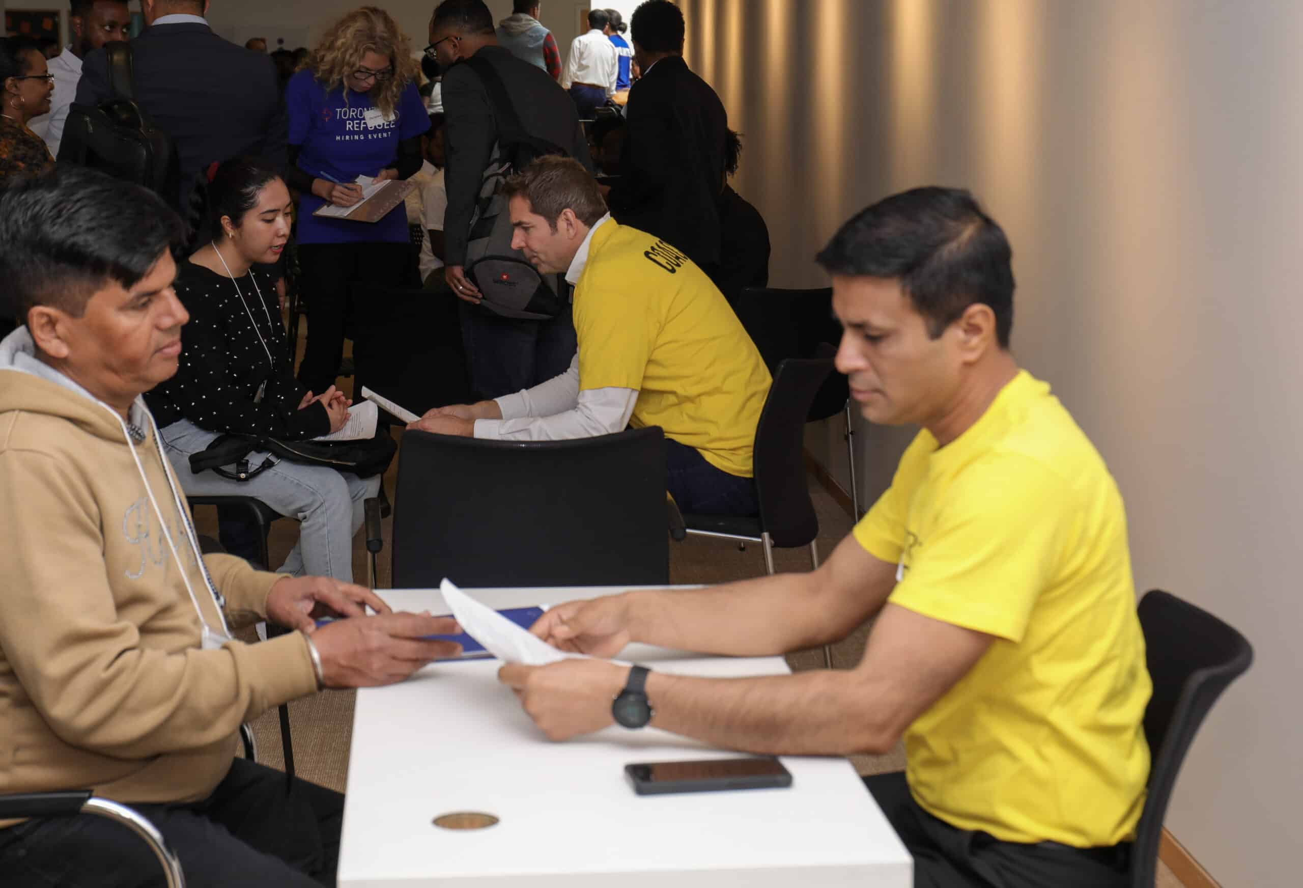 2024 jumpstart refugee talent hiring event photo at the ismaili centre featuring volunteers in yellow shirts sitting at desks one one on helping job seekers