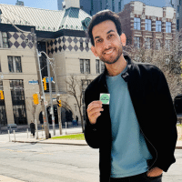 Omer stands proudly outside a polling station holding a voting sticker, smiling with quiet pride after casting his first vote as a Canadian citizen.