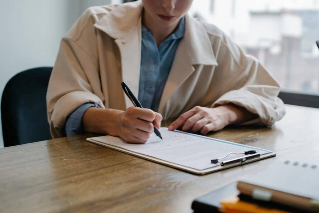 A person writing on a printed resume with a pen while sitting at a wooden desk.