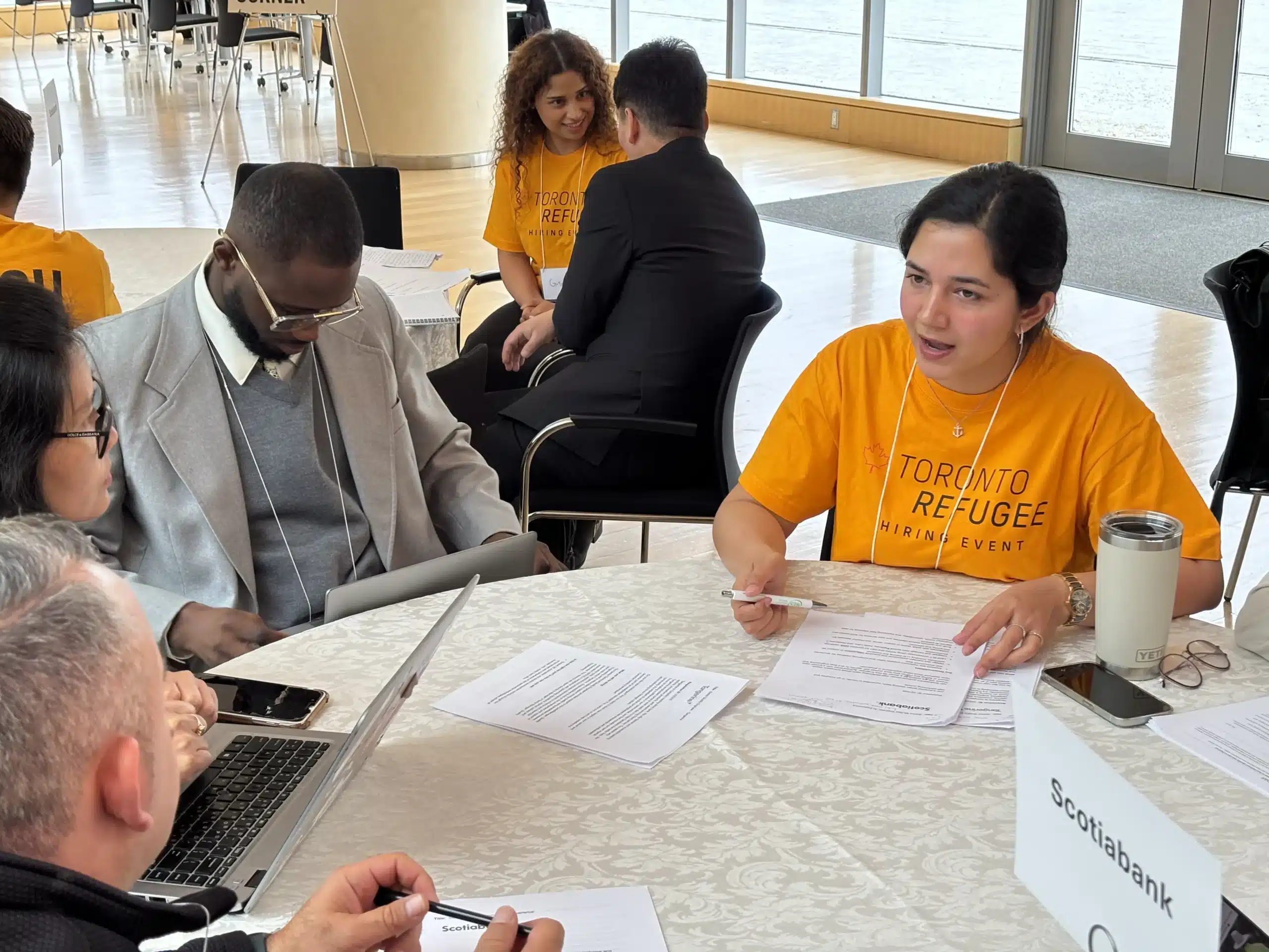 A group of clients seated around a table receiving guidance from a career coach during the Toronto Refugee Hiring Event.