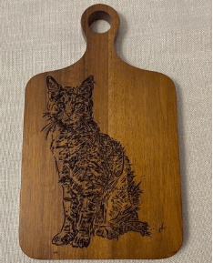 A rectangular layered wooden platter, 10 by 6 inches, displayed against a neutral background. The central design is a stylized cat figure composed of curved and intricate Arabic lettering, creating a unique visual pattern. The wood has a warm, natural grain.